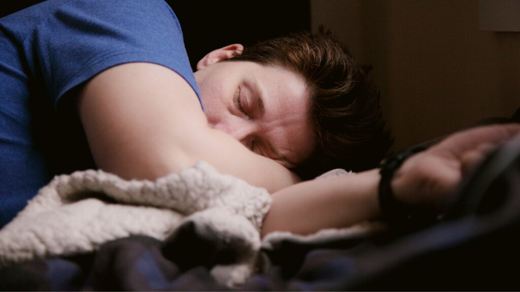 Man sleeping on his side in bed with his head resting on his arm.