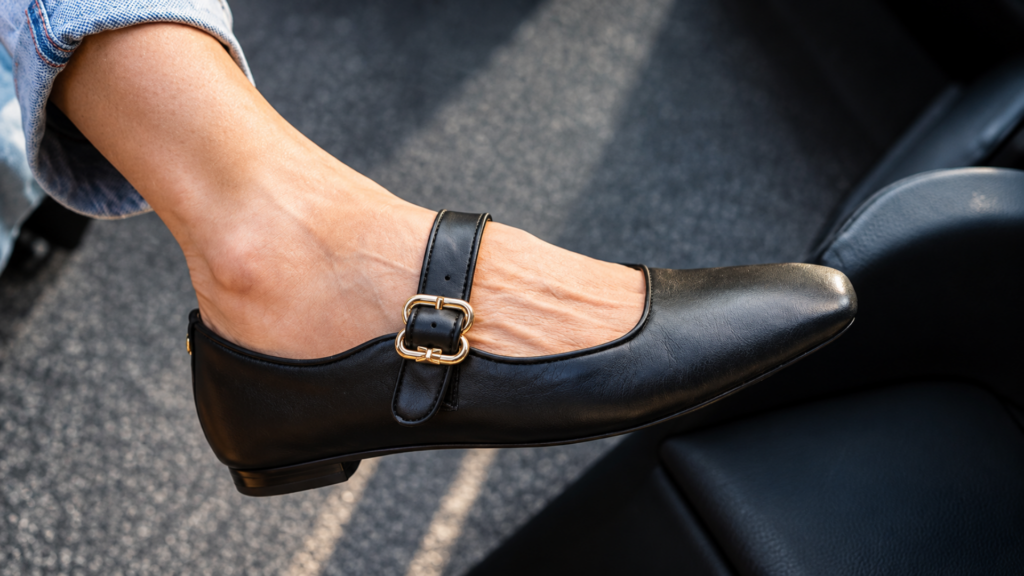 Close-up of a foot wearing a black leather Mary Jane flat with a gold buckle strap.