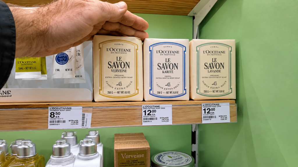 Hand reaching for packaged L'Occitane French bar soaps on a store display shelf.