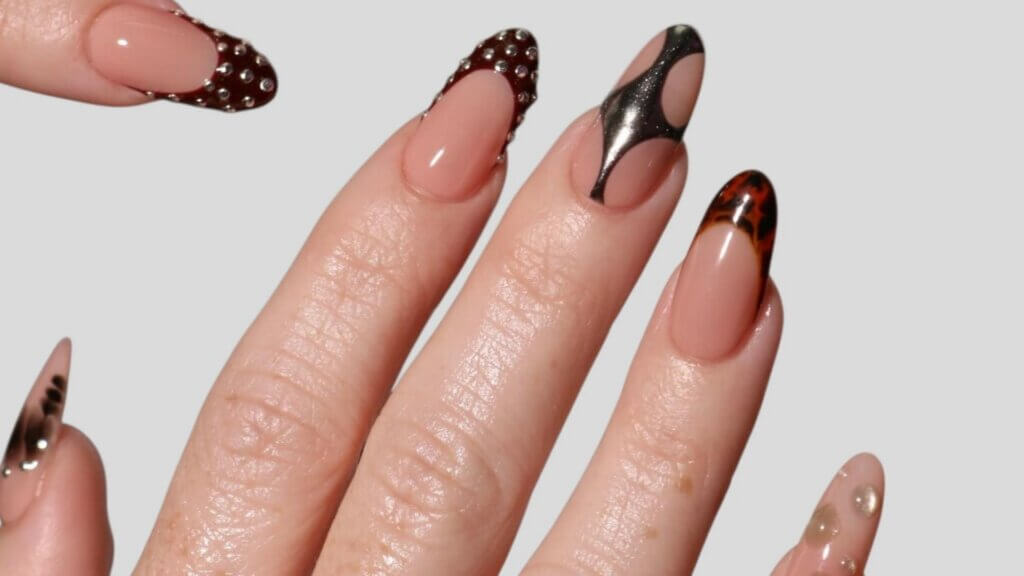 Long nude nails featuring rhinestones, metallic designs and tortoiseshell tips.