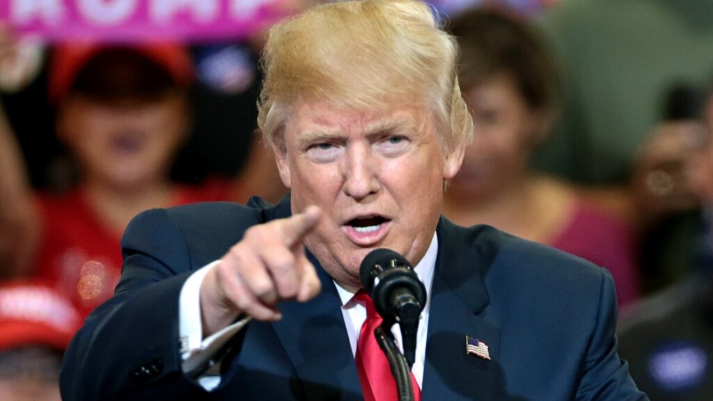 Donald Trump points toward the audience while speaking into a microphone at a campaign event.
