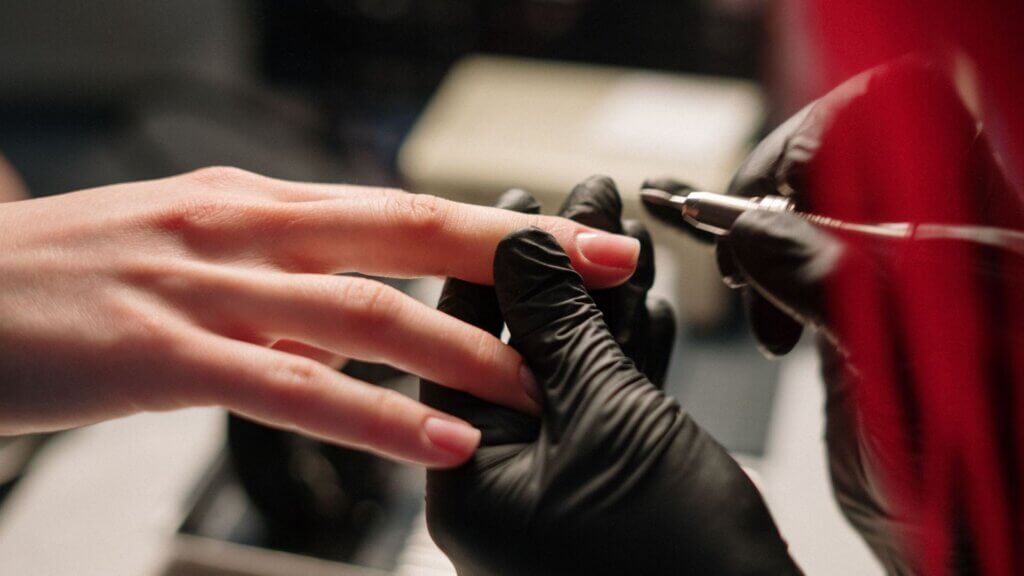 Nail technician using an electric drill to shape a client's fingernail.