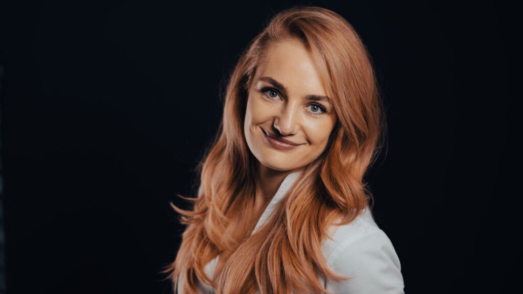 Woman with long red hair smiling for a portrait against a black background.