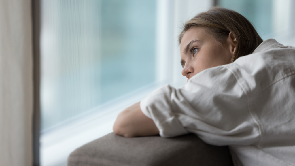 Woman resting her head on her arms while gazing out a window.