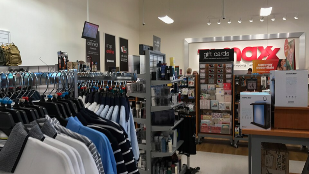 Interior view of a T.J. Maxx store showing a display of men's shirts and a gift card rack near the entrance.