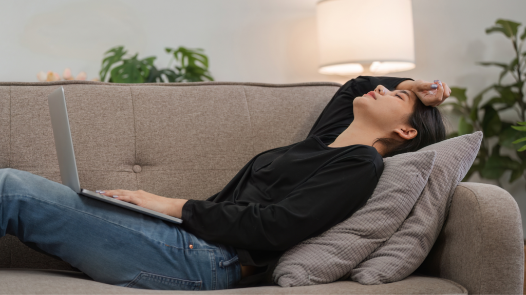 Woman lying back on a couch with her eyes closed, holding a laptop.