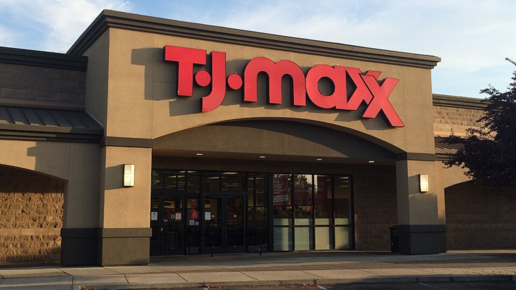 Exterior of a T.J. Maxx store with its red logo sign prominently displayed above the entrance in the late afternoon sun.