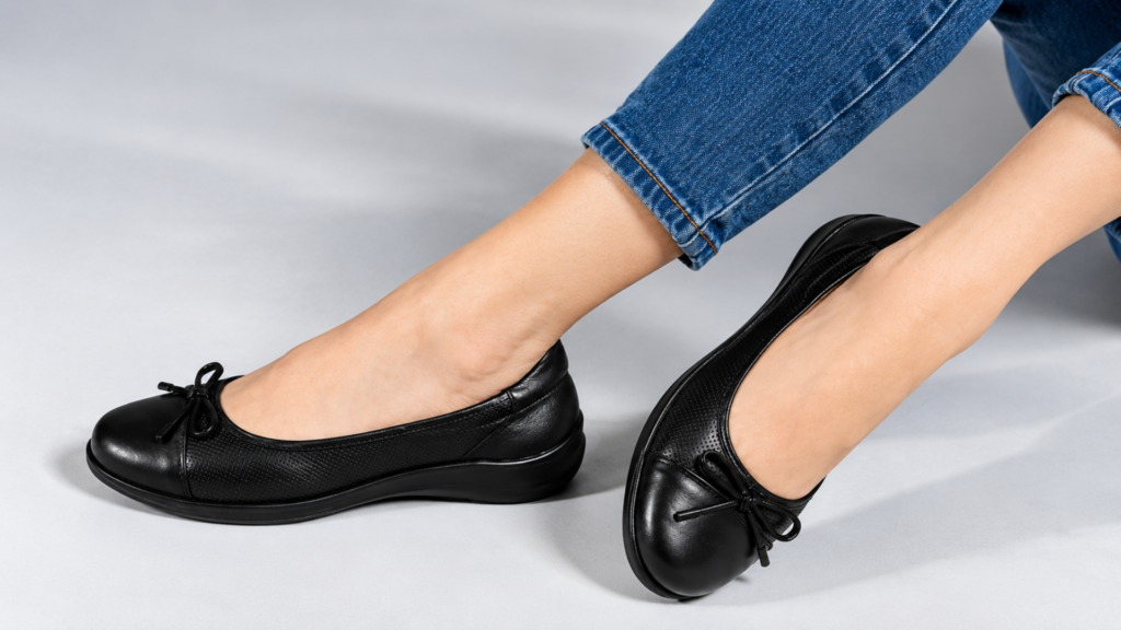 Close-up of a person wearing blue jeans and black leather ballet flats with bow details.