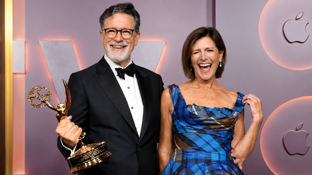 Stephen Colbert holding an Emmy Award while posing alongside his wife Evelyn McGee-Colbert on a red carpet.