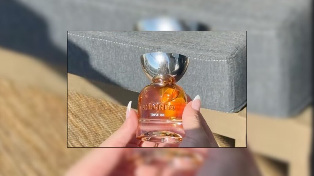 Cécred Temple Oud Hair Perfume bottle held in a hand, showing the amber-colored fragrance and silver cap in natural sunlight.