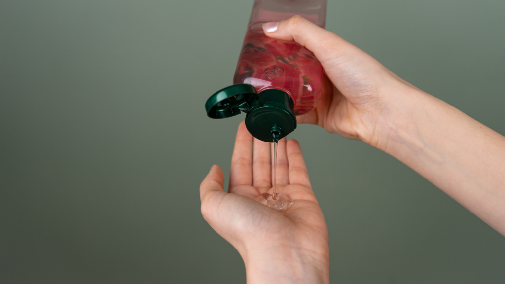 A person pours a stream of clear liquid from a translucent bottle with a green cap into their open palm.