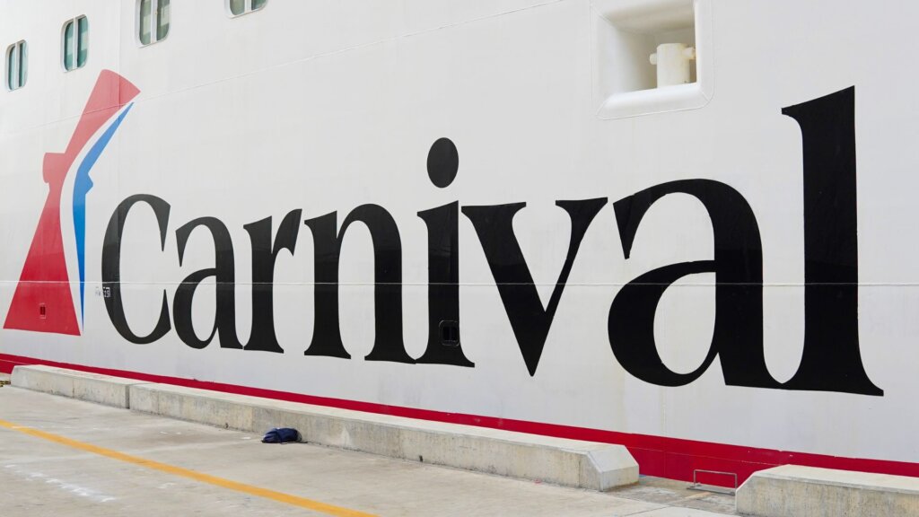 Close-up of a white Carnival cruise ship hull with large black “Carnival” lettering and its red-and-blue logo.