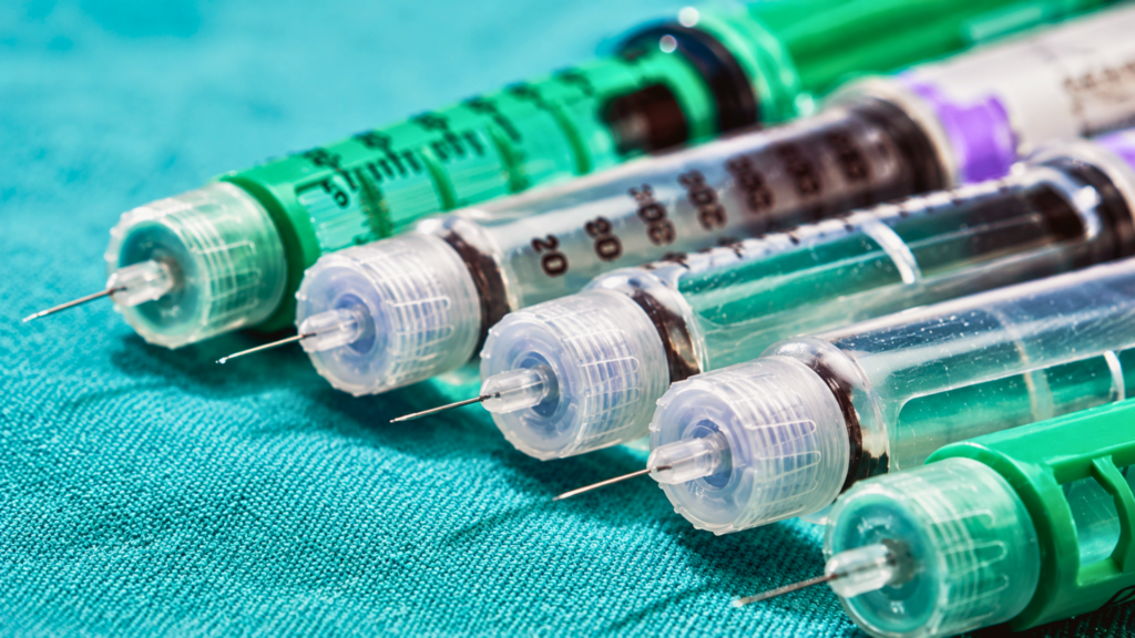 A row of medical insulin pen injectors lined up on a green surgical fabric background.