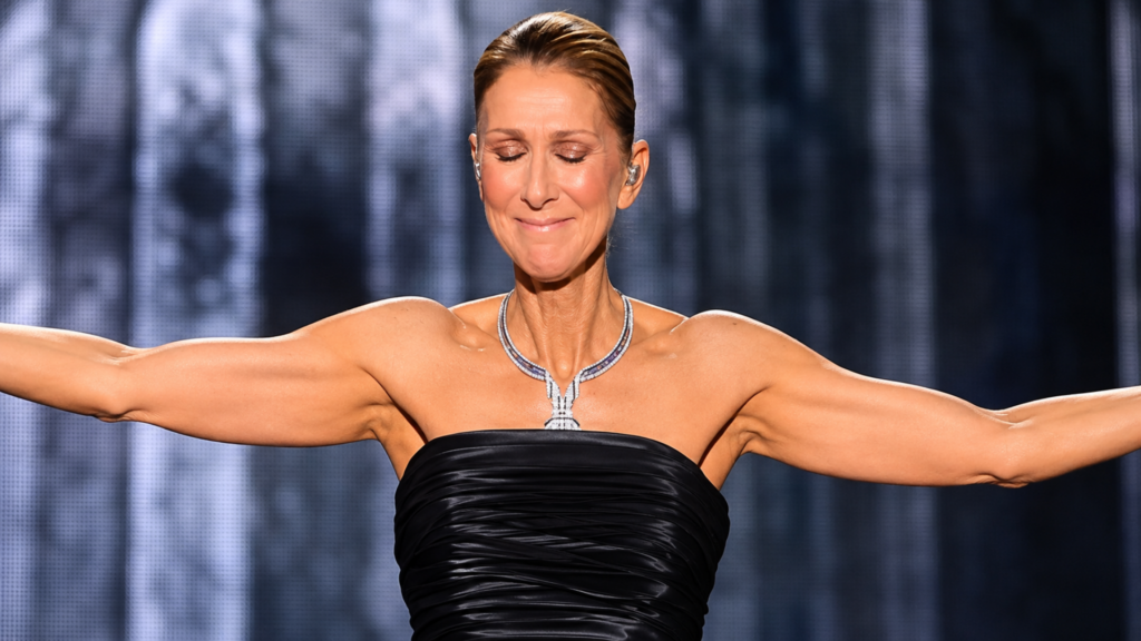 Celine Dion in a black strapless gown with her arms outstretched during a performance.