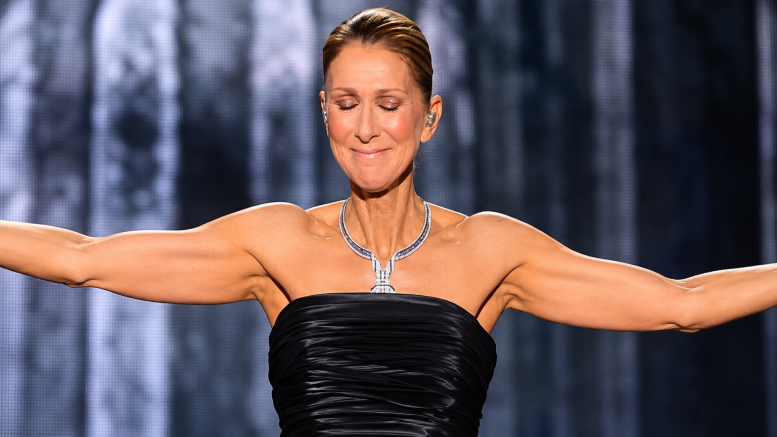 Celine Dion in a black strapless gown with her arms outstretched during a performance.