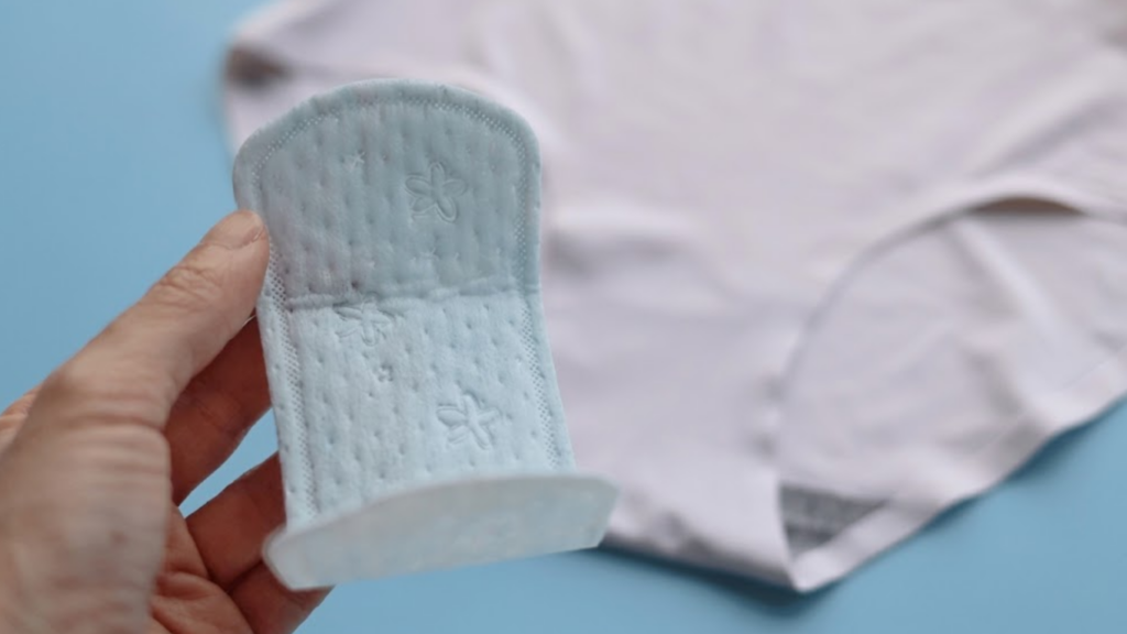 Women's hand holding panty liner pad with white women's panty in blue background.
