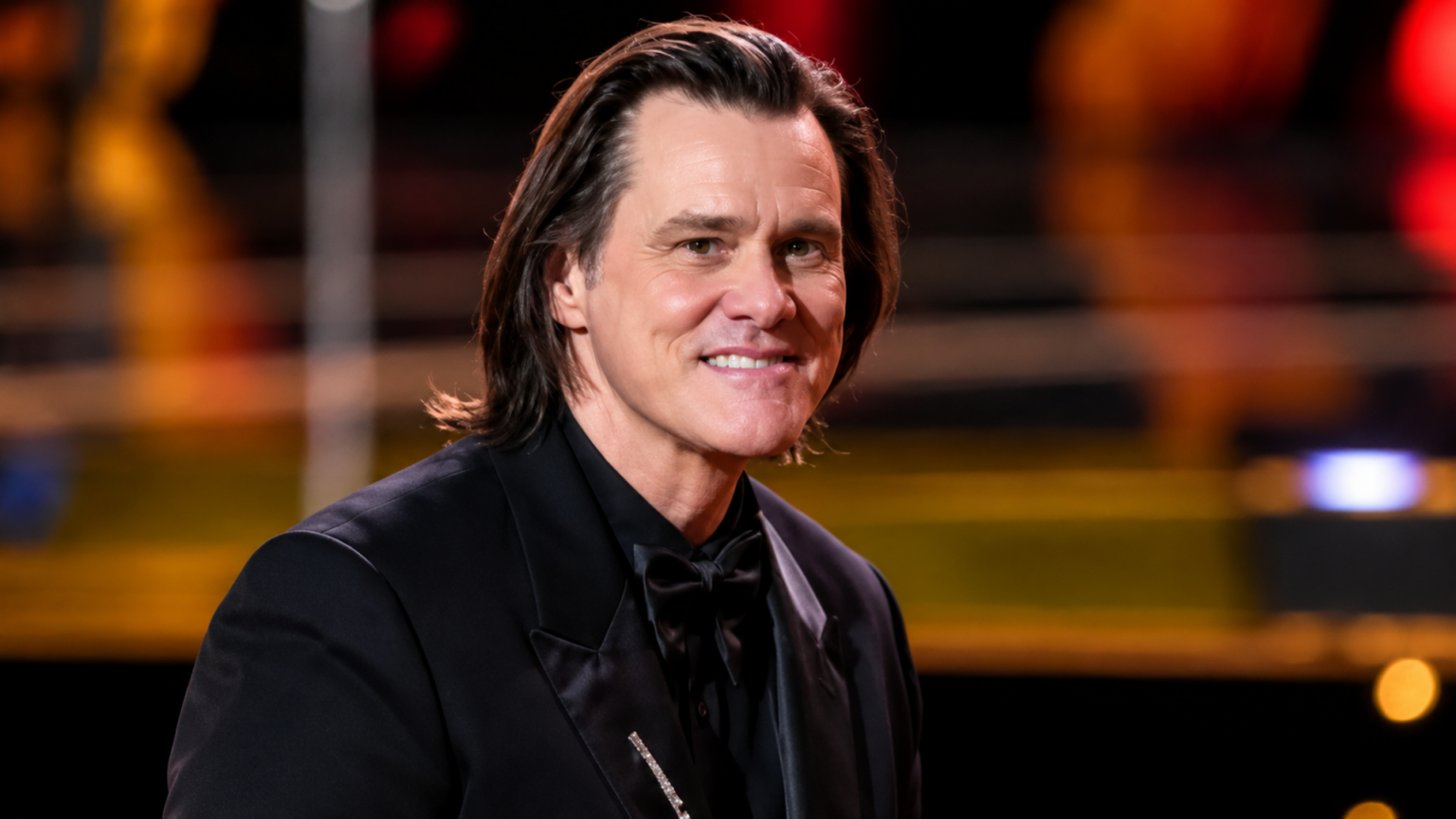 Jim Carrey Is a Married Man Again for the Third Time and Some People Have a Problem With It Actor Jim Carrey wearing a black tuxedo with a bow tie smiling on stage.