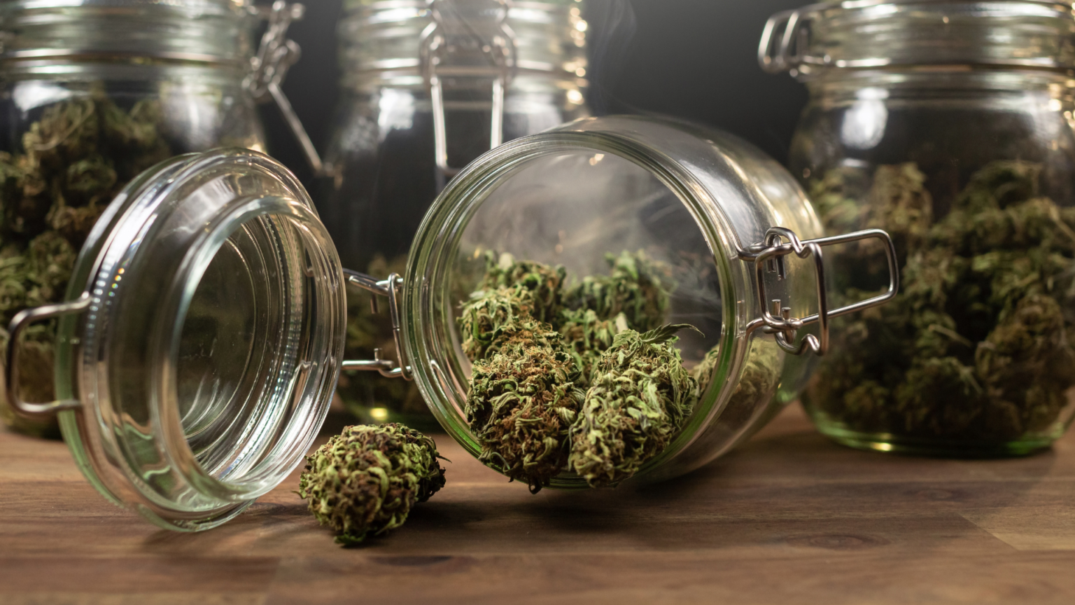Glass jars filled with dried cannabis buds on a wooden surface.