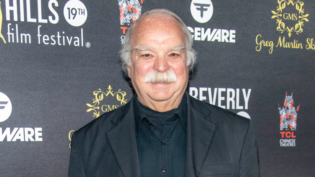 Richard Riehle smiling on a red carpet with a film festival backdrop.
