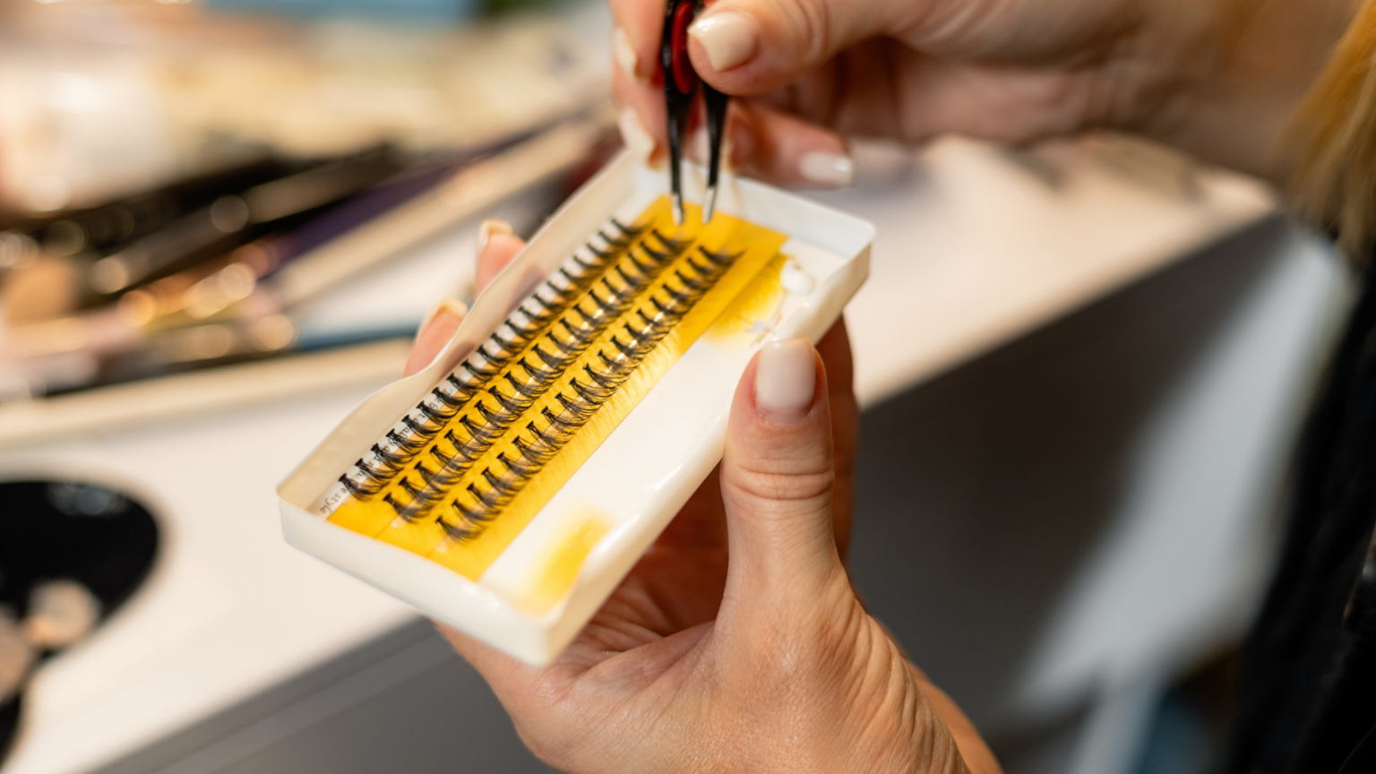 Holding a tray of individual false eyelashes with tweezers.