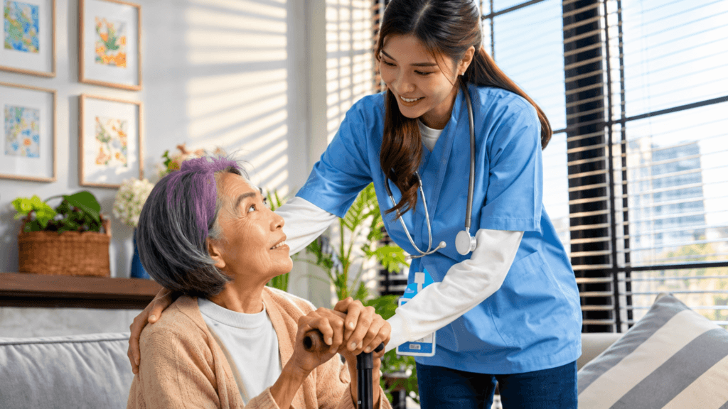 A healthcare worker in blue scrubs resting a hand on an elderly woman holding a walking cane.
