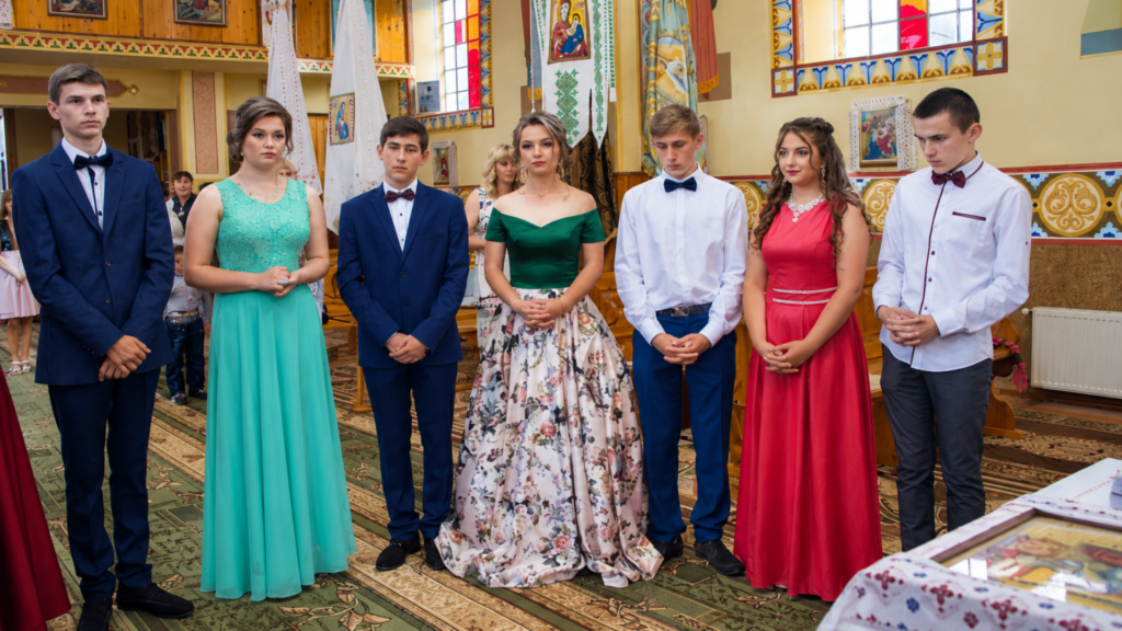 A group of smartly dressed young men and women standing in formal attire inside a church setting.