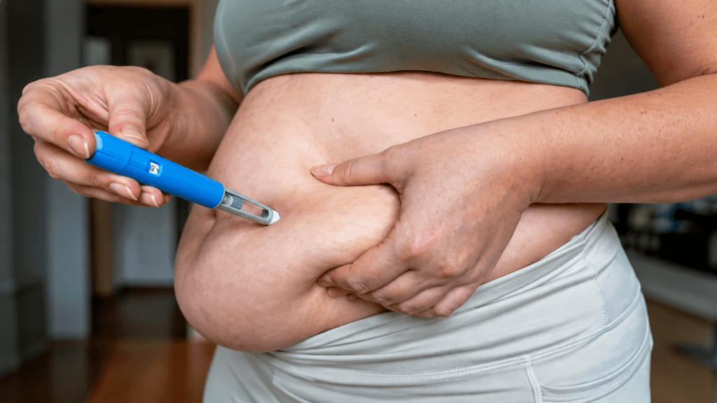 A person holding a blue pen-style injector against their abdomen to administer medication.