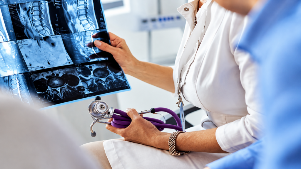 Doctor holding a purple stethoscope while examining spine MRI scans with colleagues.