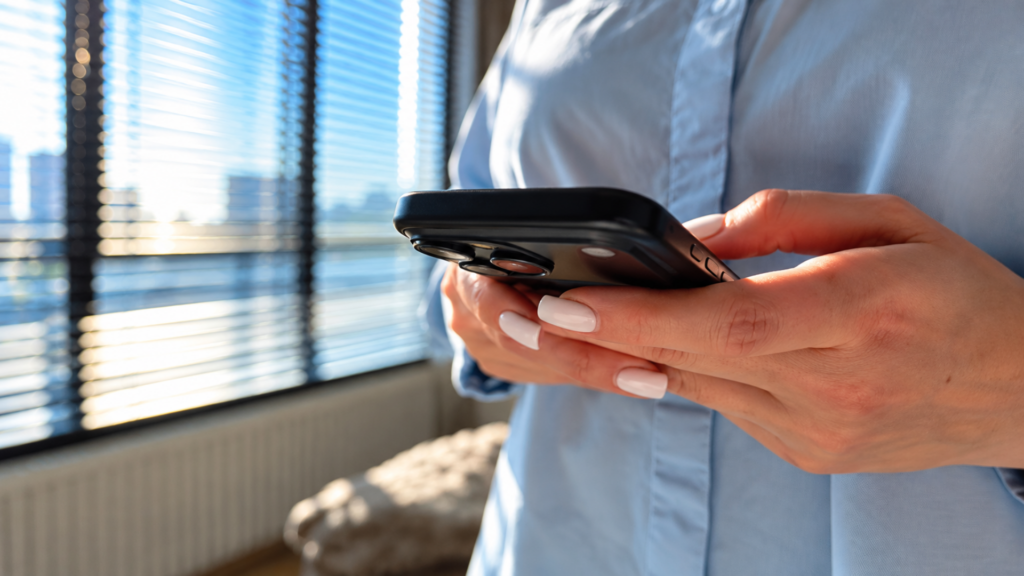Close-up of a person with manicured nails holding and typing on a smartphone indoors.