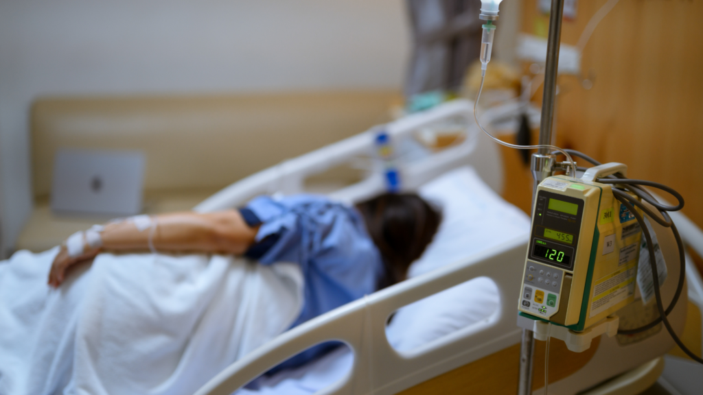 Patient lying in a hospital bed connected to an IV infusion pump.