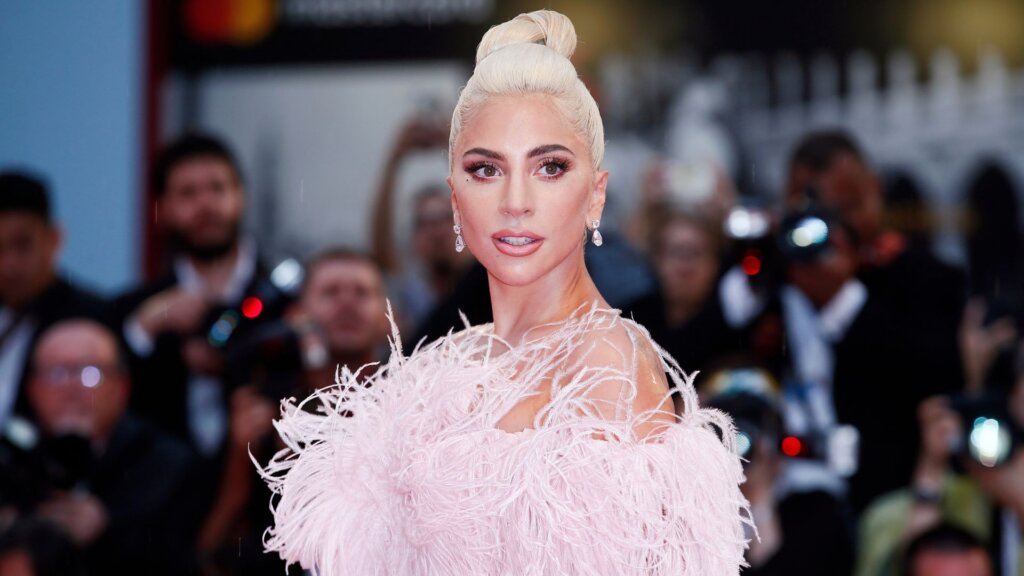 Lady Gaga in a pale pink feathered gown posing on a red carpet.