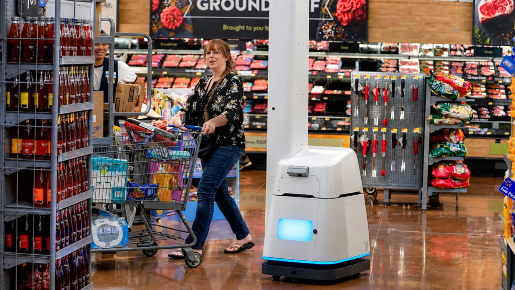A shopper pushing a shopping cart past an autonomous scanning robot navigating a grocery store aisle.