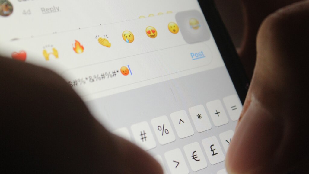 Close-up of a smartphone screen showing an angry emoji, reaction options, and a comment filled with symbols representing disappointment and anger.