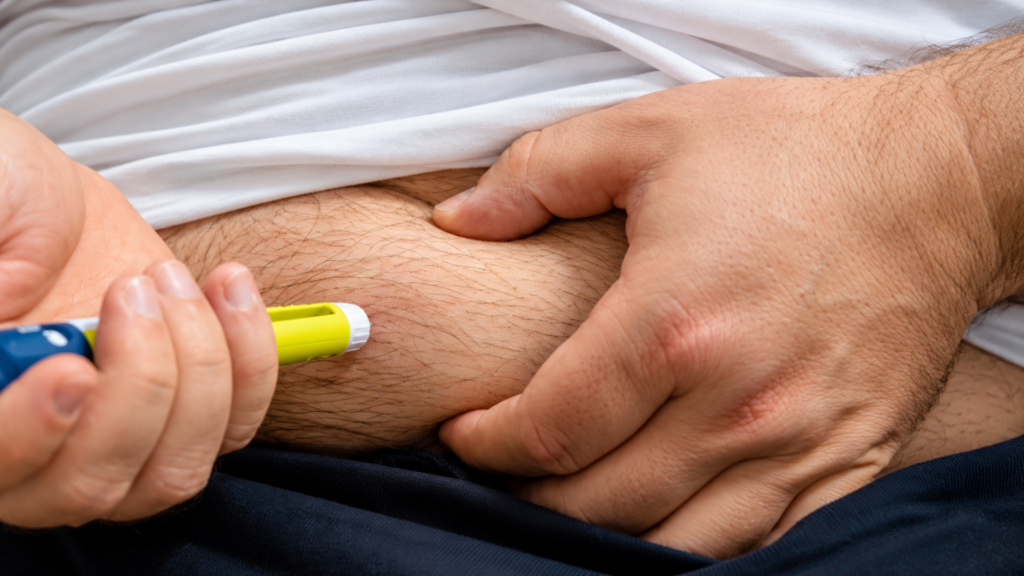 A man holding a yellow and blue injector pen against his abdomen to administer a subcutaneous injection.