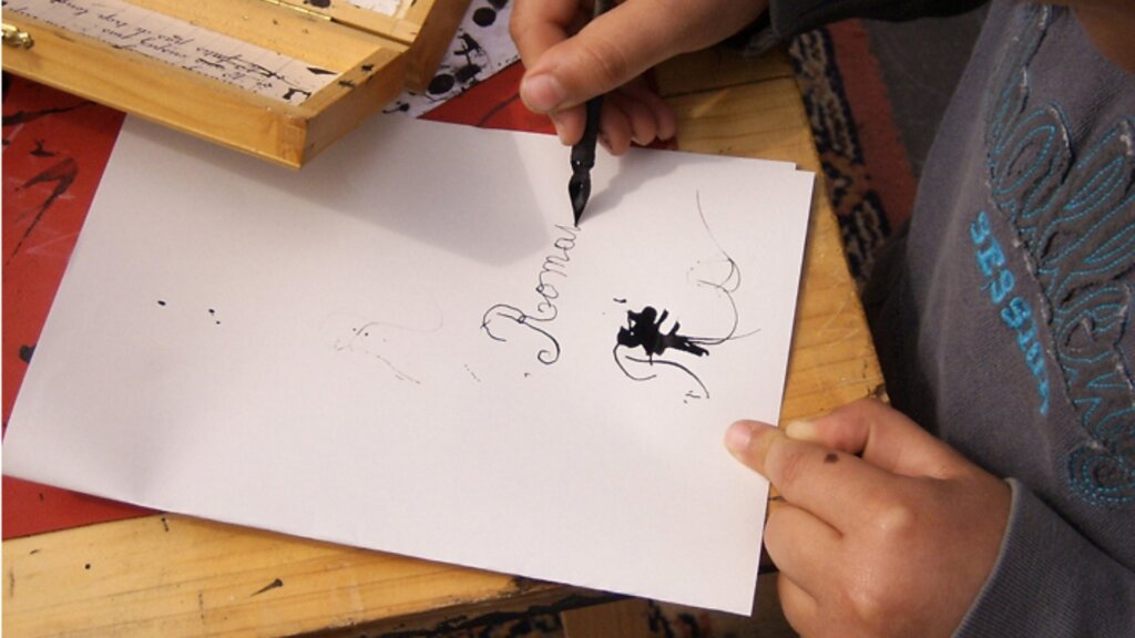 A child practices cursive handwriting with a fountain pen on a sheet of white paper.
