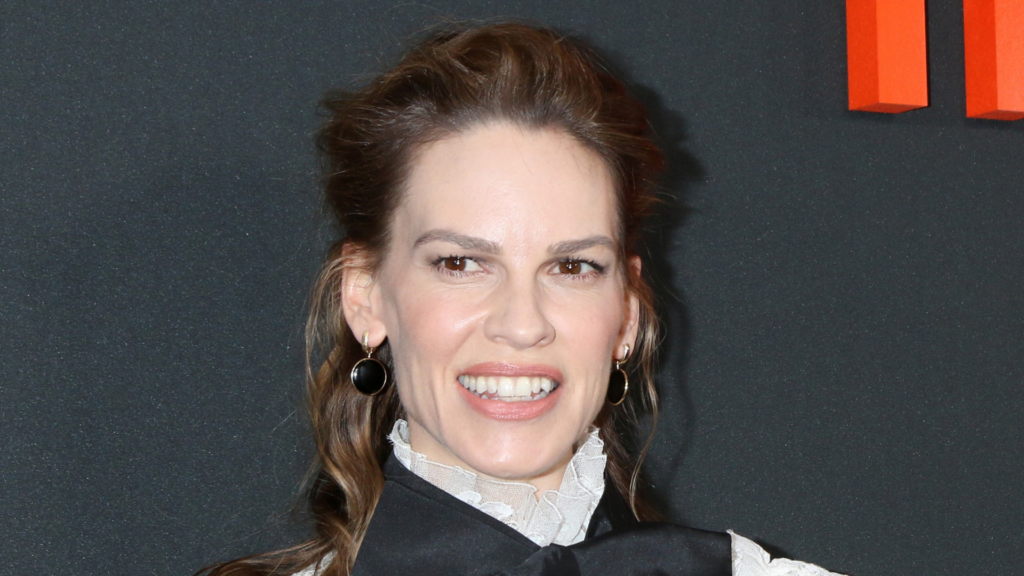 Hilary Swank smiling in a high-collared black dress.