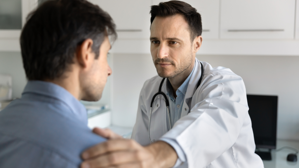 Doctor placing a supportive hand on a male patient's shoulder during a consultation.