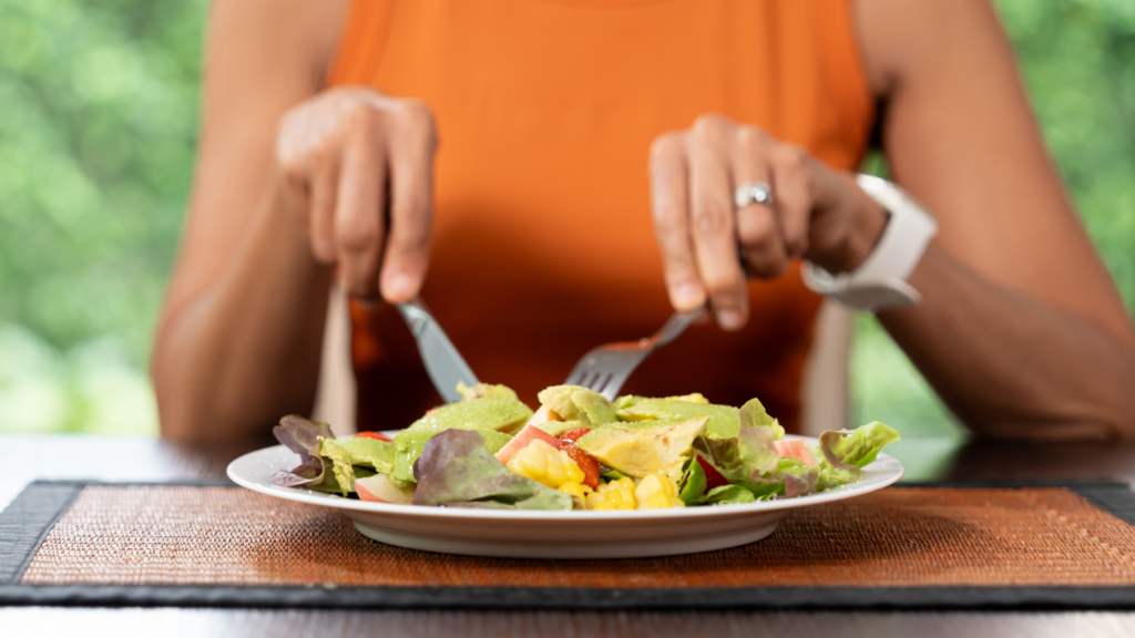 Person eating a fresh avocado salad with a fork and knife.