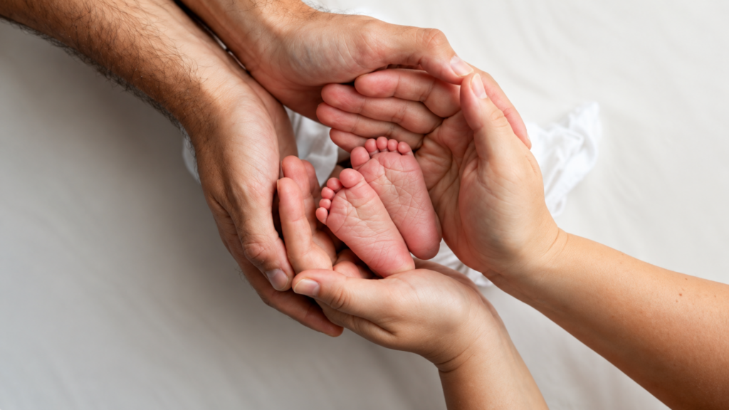 An overhead view of parents cradling their newborn baby's tiny feet in their hands.