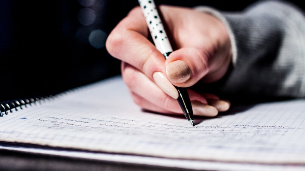 Close-up of a person writing by hand with a pen in a lined notebook.