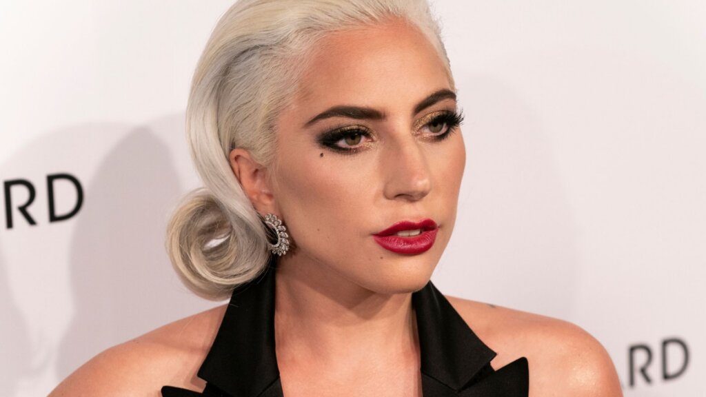 Lady Gaga wearing bold red lipstick, smoky eye makeup, and a black halter outfit.