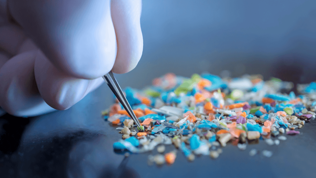 Gloved hand using tweezers to sort through colorful microplastics.