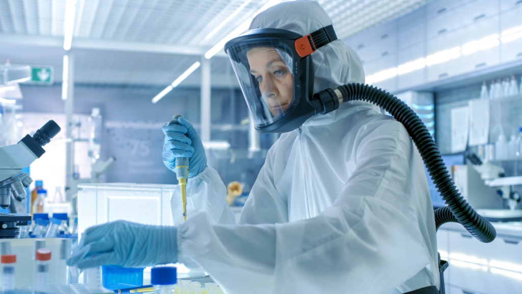 Healthcare worker in a hazmat suit using a pipette in a laboratory.