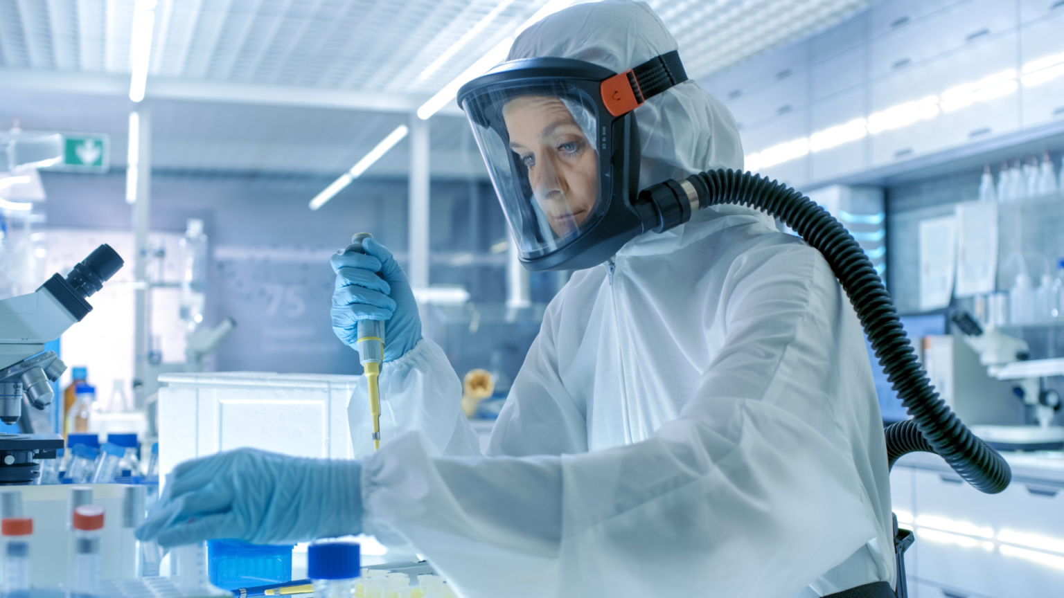 Healthcare worker in a hazmat suit using a pipette in a laboratory.