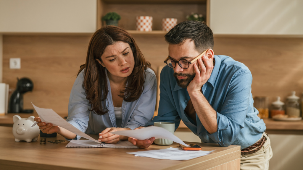 A concerned couple reviewing financial documents at a kitchen counter.