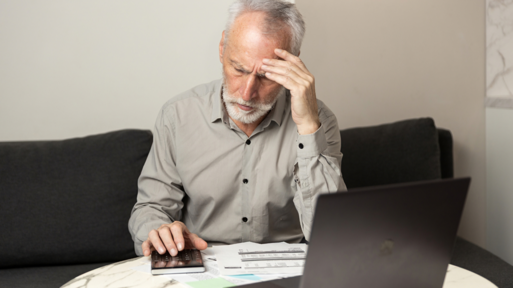 Stressed older man reviewing paperwork with a calculator.