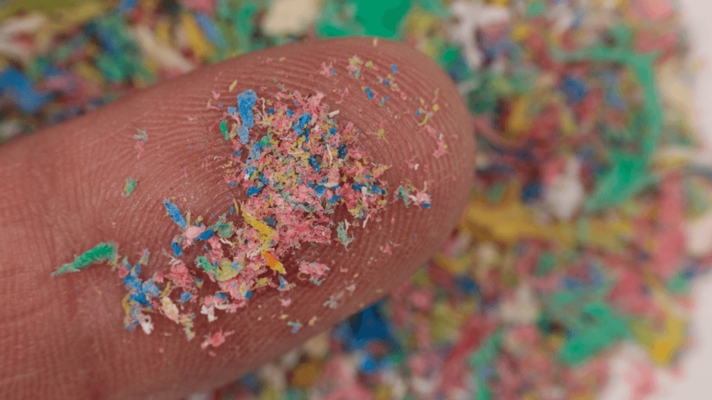 Close-up of a fingertip covered in tiny, colorful microplastic particles.