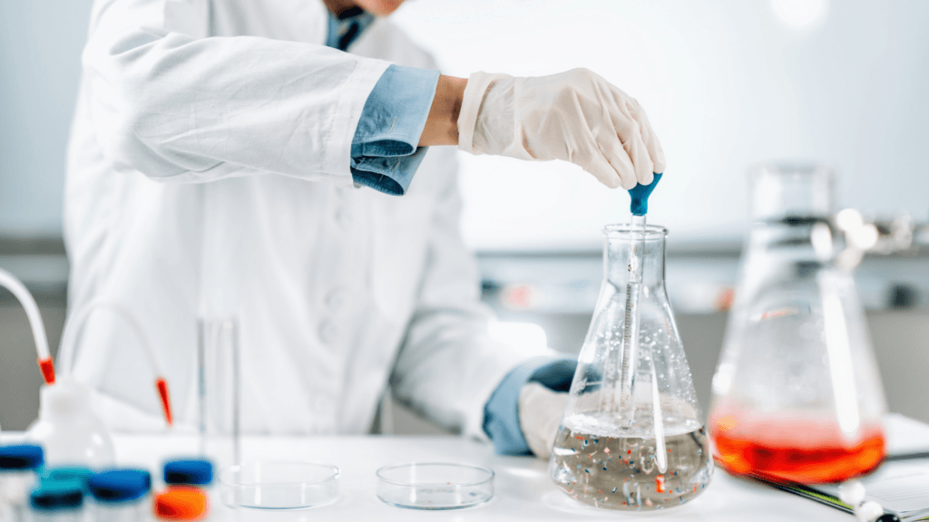 Scientist in a lab using a pipette on a flask containing microplastics.