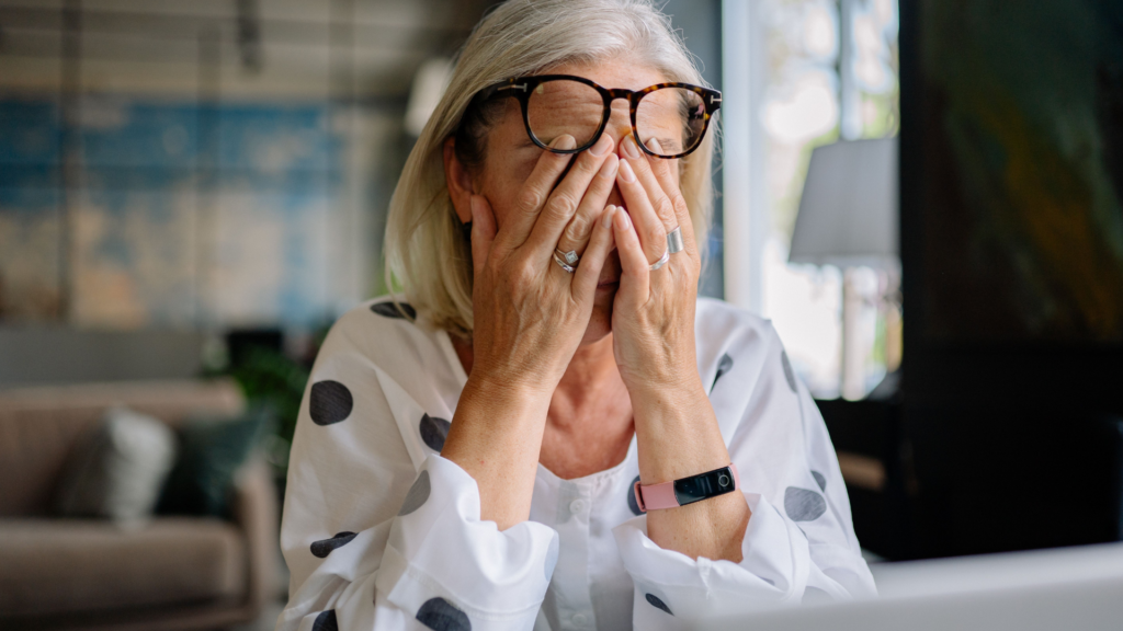 Senior woman experiencing stress indoors, covering face with hands. Reflects emotion and solitude.