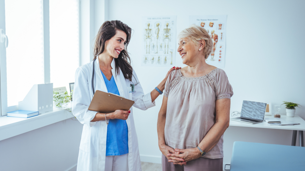 Female doctor holding a clipboard and placing a comforting hand on an elderly patient's shoulder.